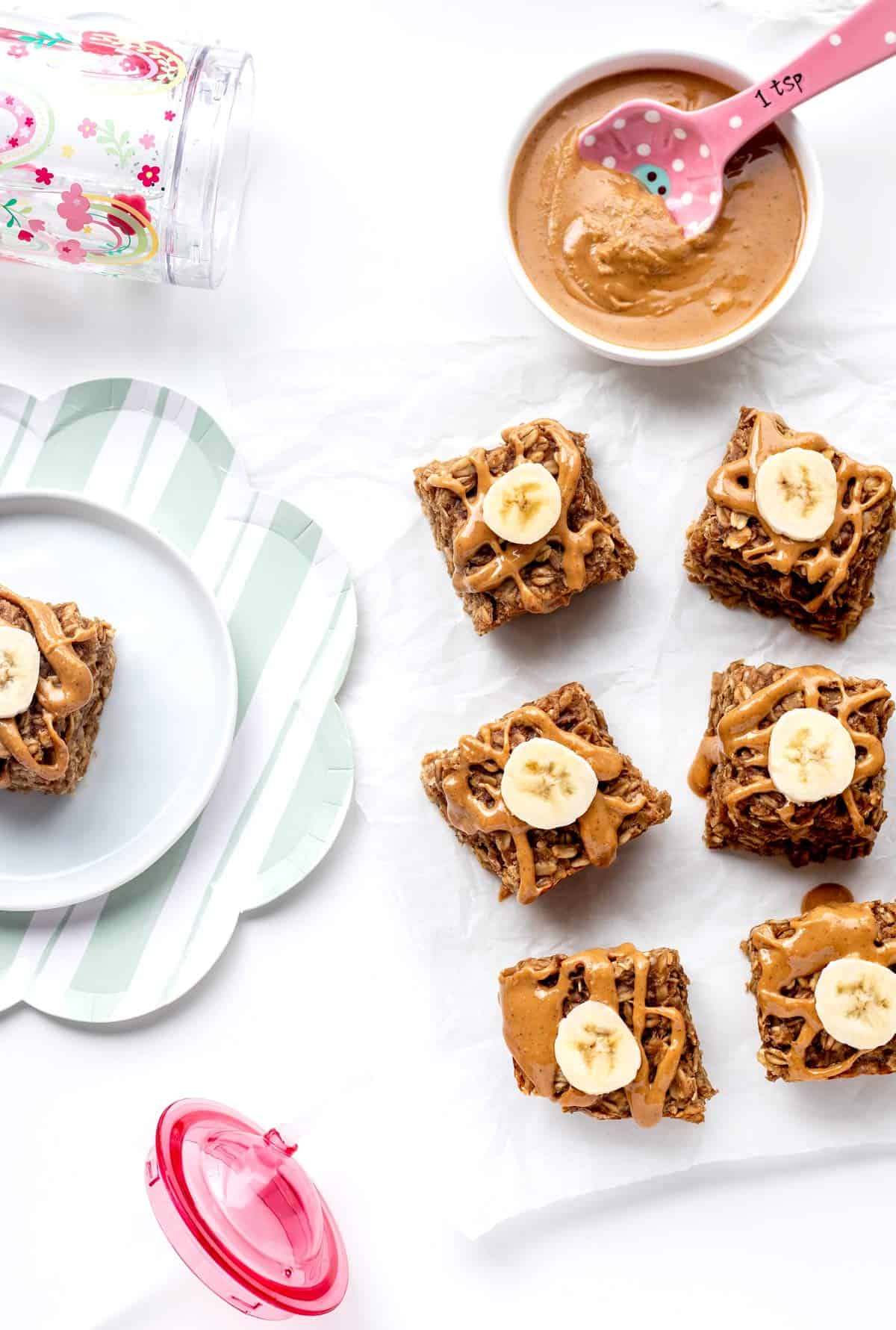 Soft-baked banana oatmeal bars next to a bowl of peanut butter.