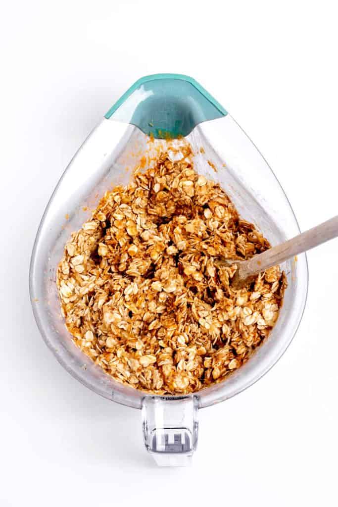 Oats, peanut butter and mashed bananas being mixed together in a measuring cup with a wooden spoon.