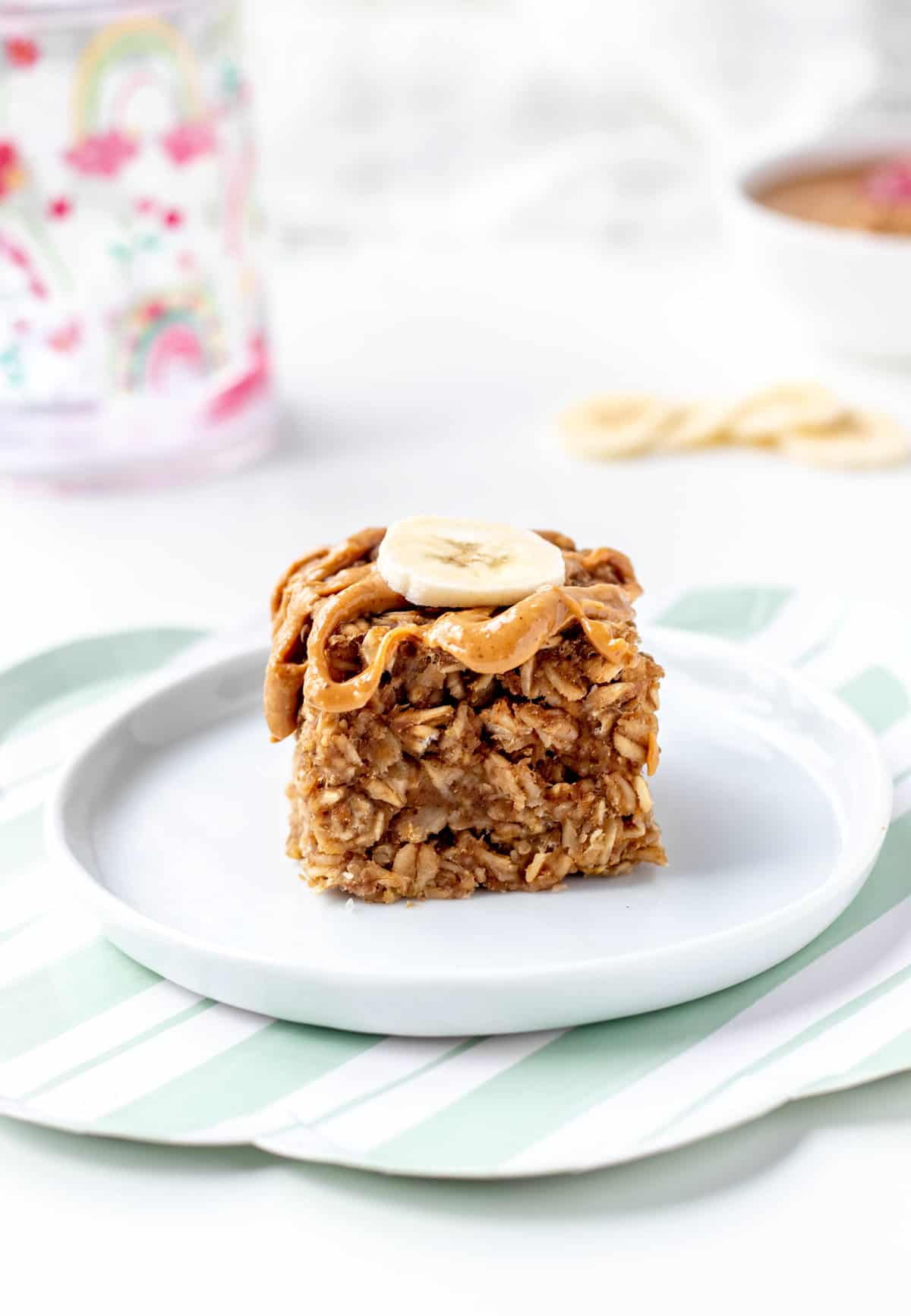 A 3-ingredient banana oatmeal bar on a white plate topped with a banana slice and peanut butter.