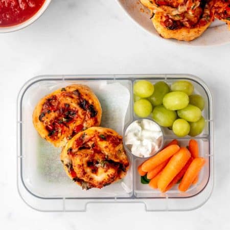 Air fryer pizza rolls in a lunch box with grapes and carrots.