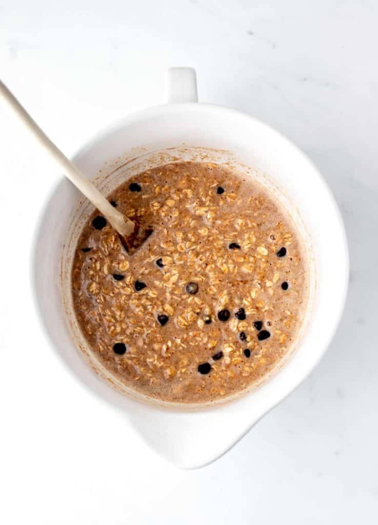 Chocolate chips added to the baked oatmeal mixture in a bowl with a wooden spoon.