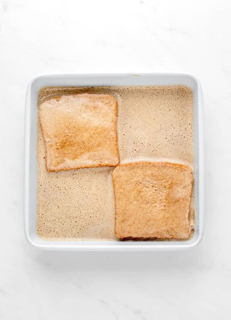 Two pieces of bread being dipped in the banana French toast mixture.