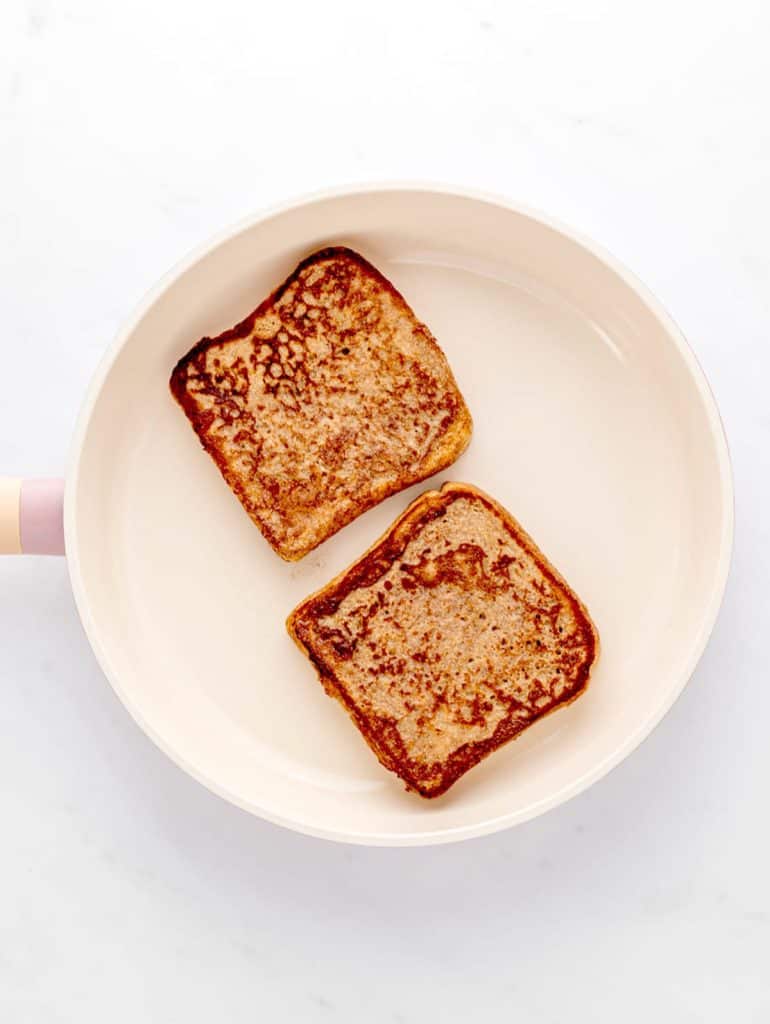 Two pieces of banana French toast being cooked in a frying pan.