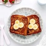 Two slices of banana French toast on a blue and white plate topped with banana slices.