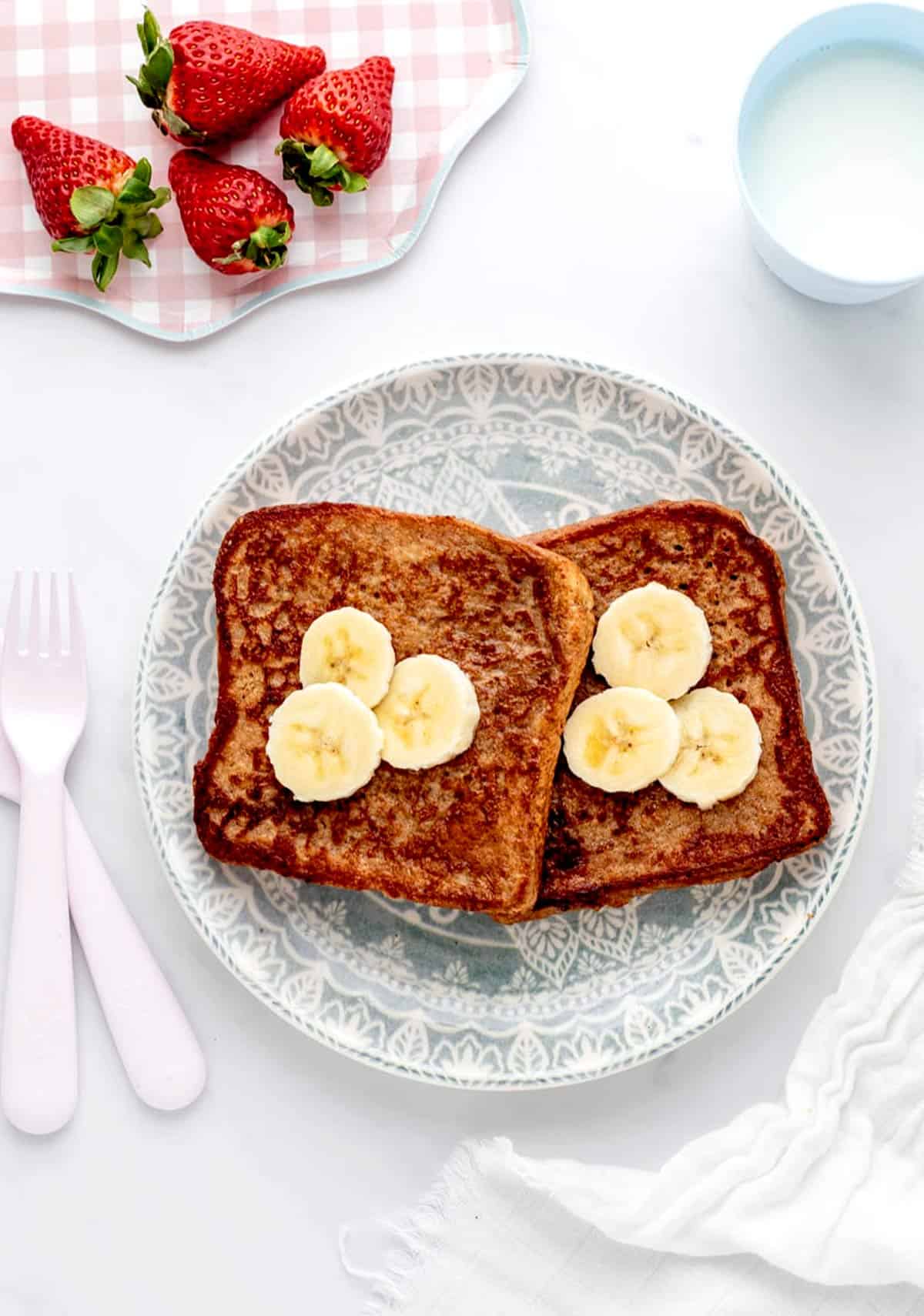 Two pieces of banana French toast on a plate topped with banana slices.