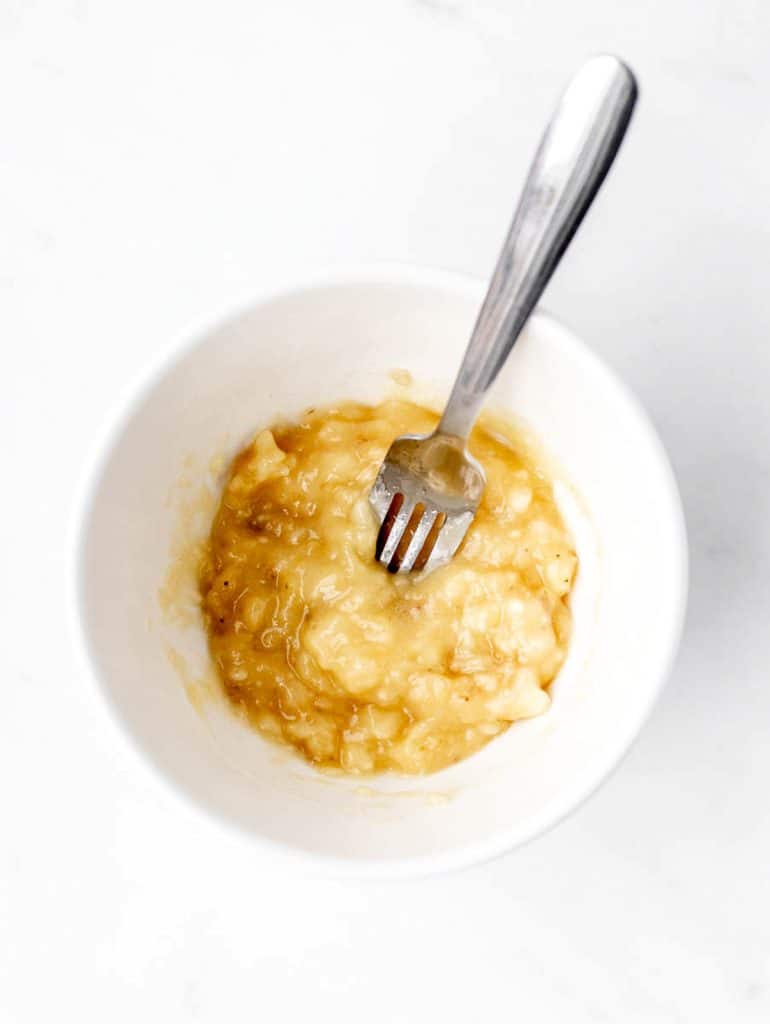 Mashed banana in a white bowl with a fork.