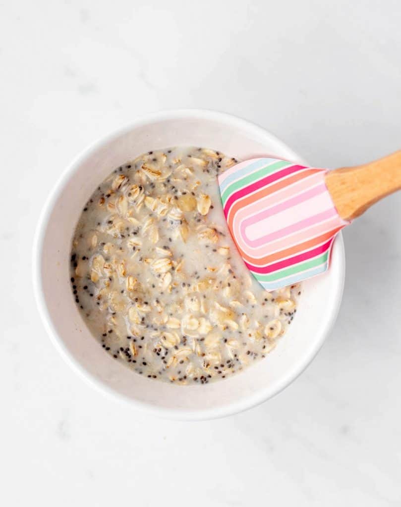 The ingredients for the BLW overnight oats being stirred together in a white bowl with a spatula.