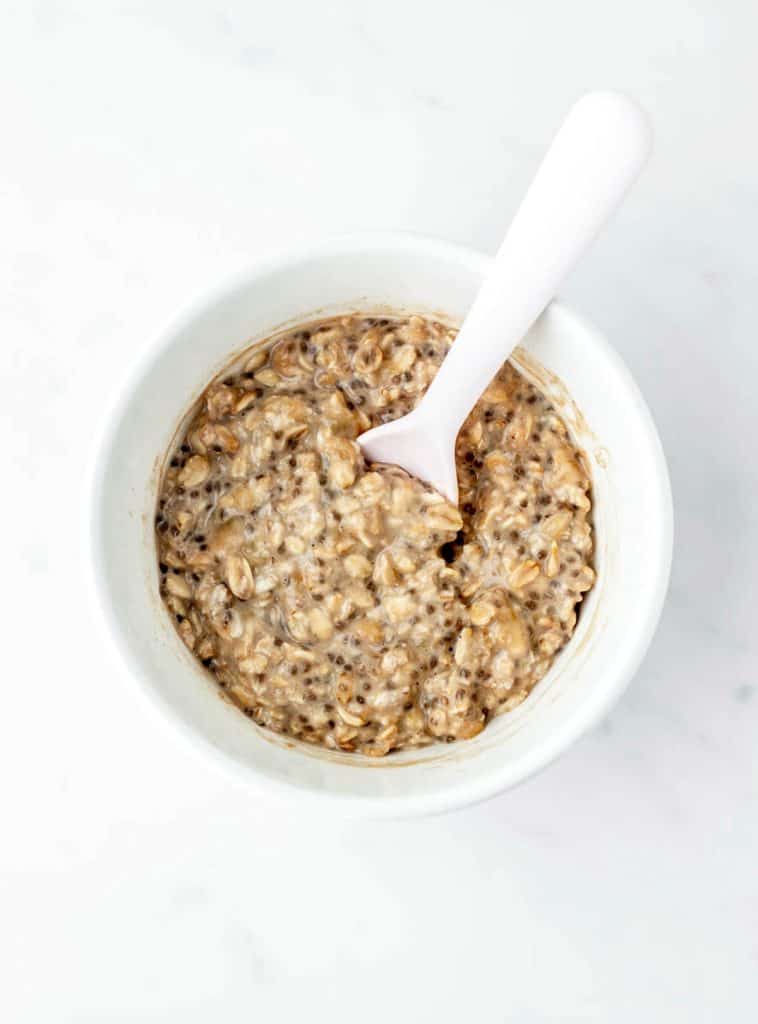 The finished overnight oats for baby in a white bowl with a spoon.