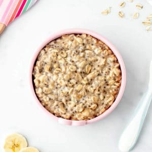 BLW overnight oats in a pink bowl next to a spoon and banana slices.