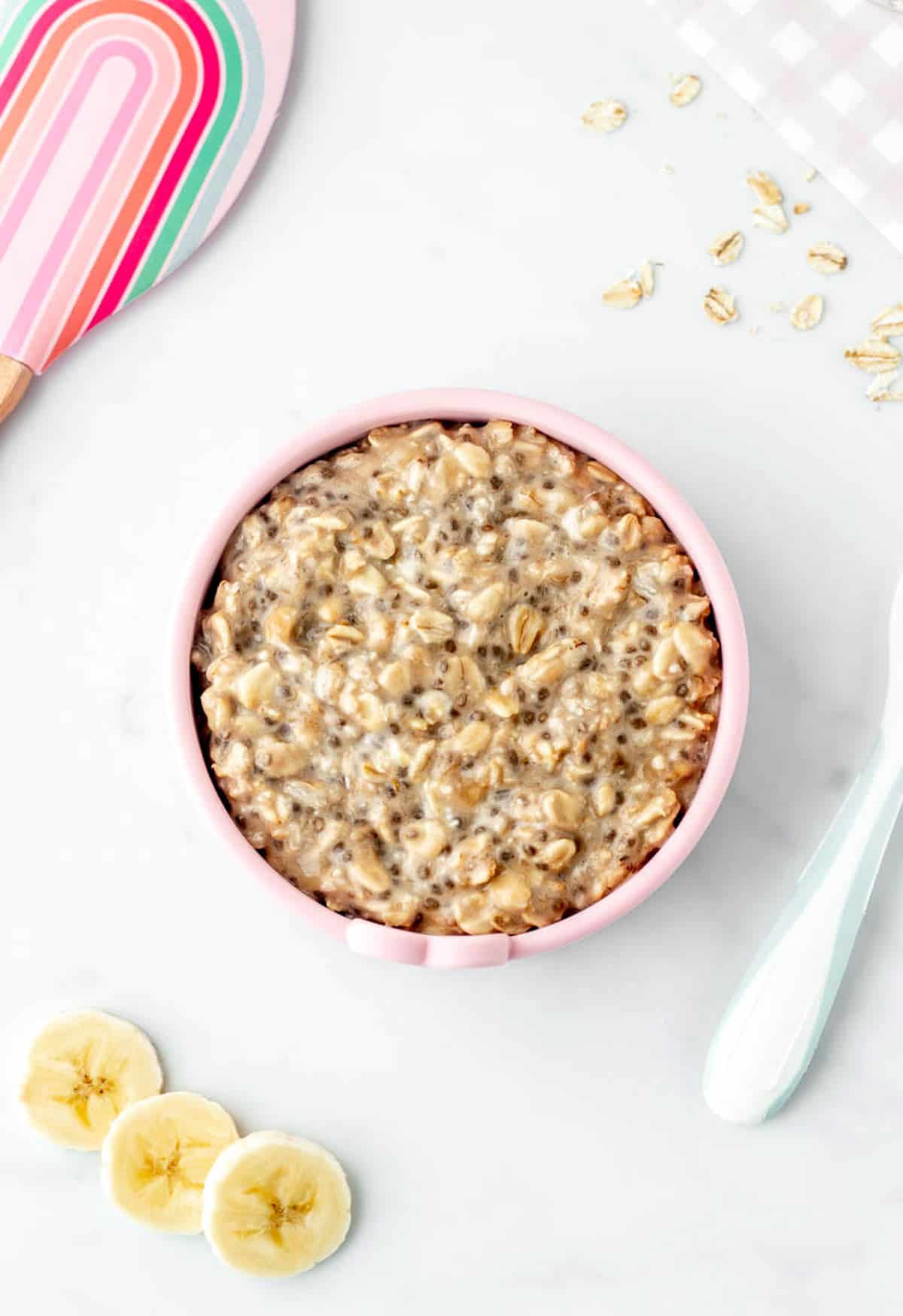 BLW overnight oats in a pink bowl next to some banana slices.