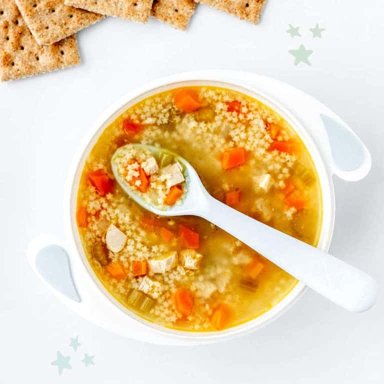 A spoon resting in a bowl of chicken pastina soup.