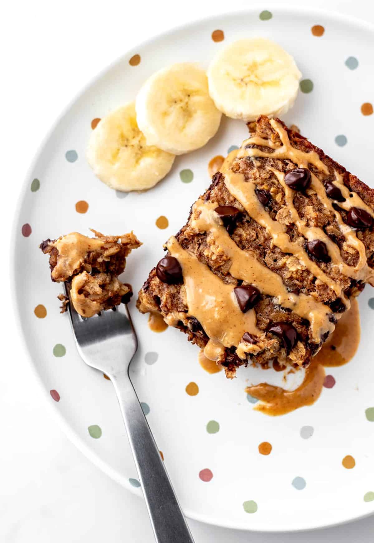 An overhead image of the baked oatmeal next to some bananas slices and a fork with some baked oatmeal on it.