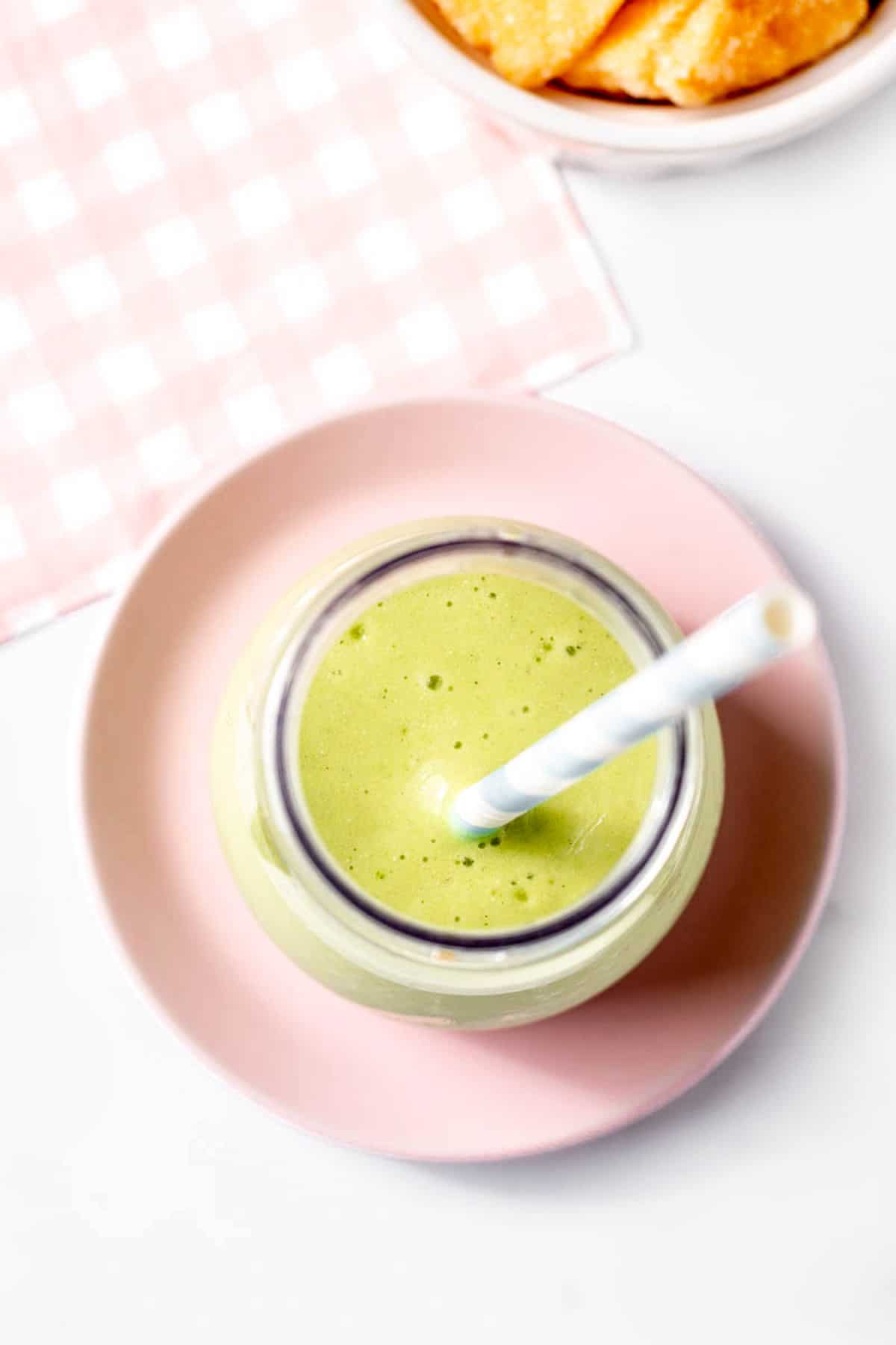 Overhead shot of a creamy green smoothie in a milk bottle with a straw.