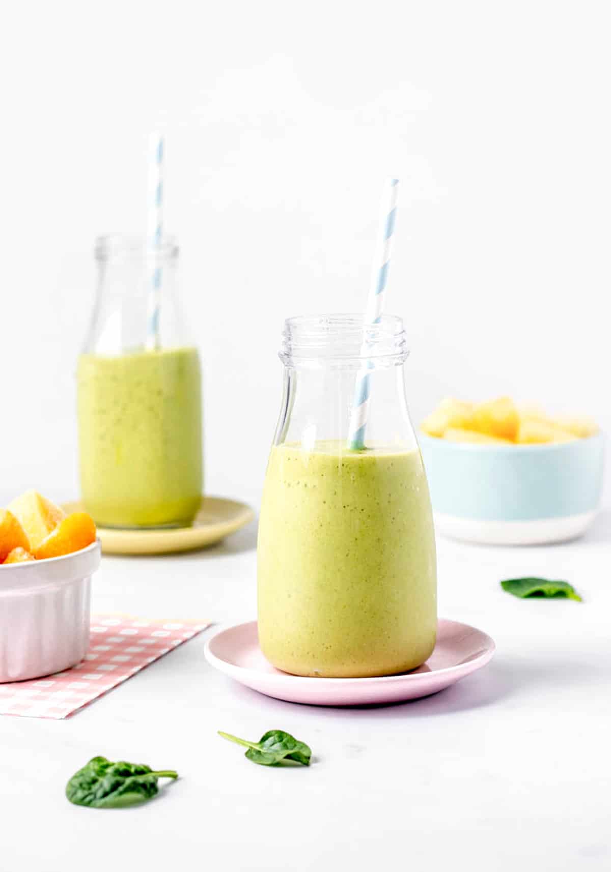 Two milk bottles with tropical green smoothie and straws.