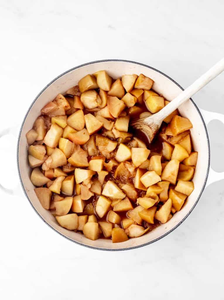 Cooked chopped apples in a pot with a wooden spoon.