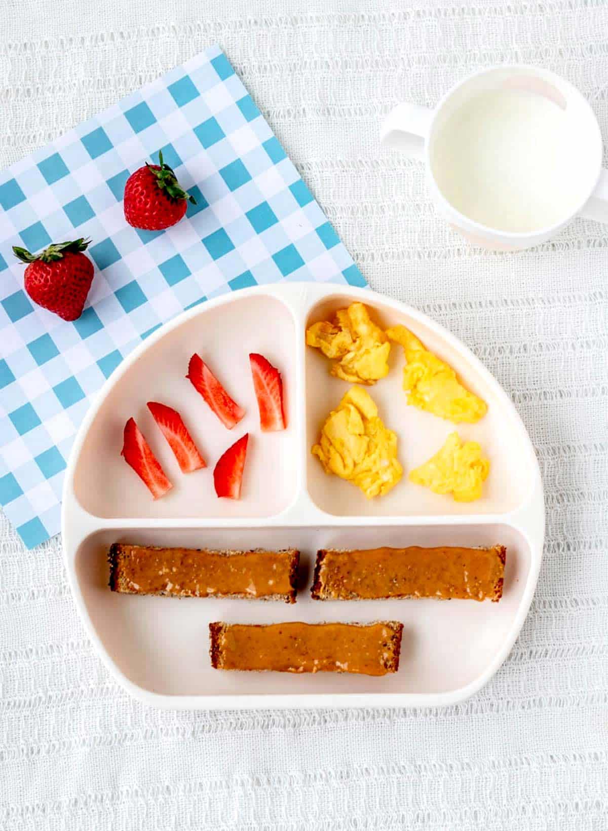 A divided plate with toast strips, sliced strawberries and scrambled eggs for baby.