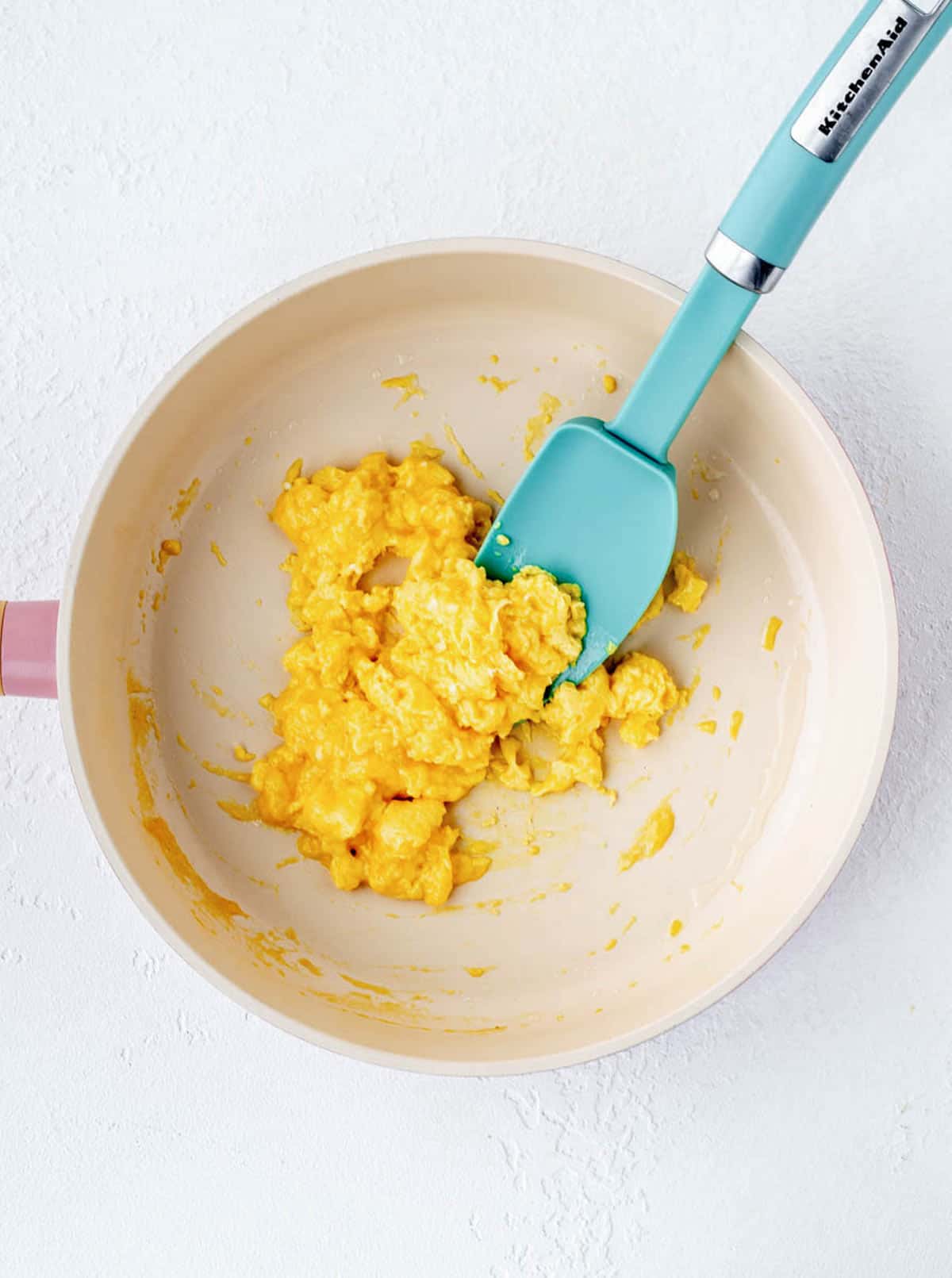 A blue spatula in a frying pan cooking scrambled eggs for baby.