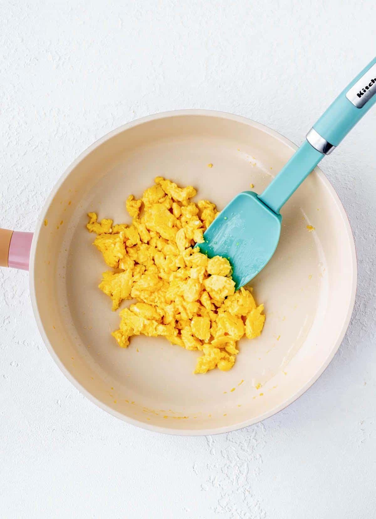 A spatula in a frying pan with cooked scrambled eggs.