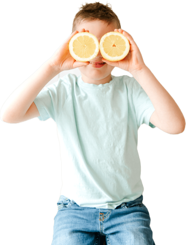 Young boy holding lemons in front of his face.