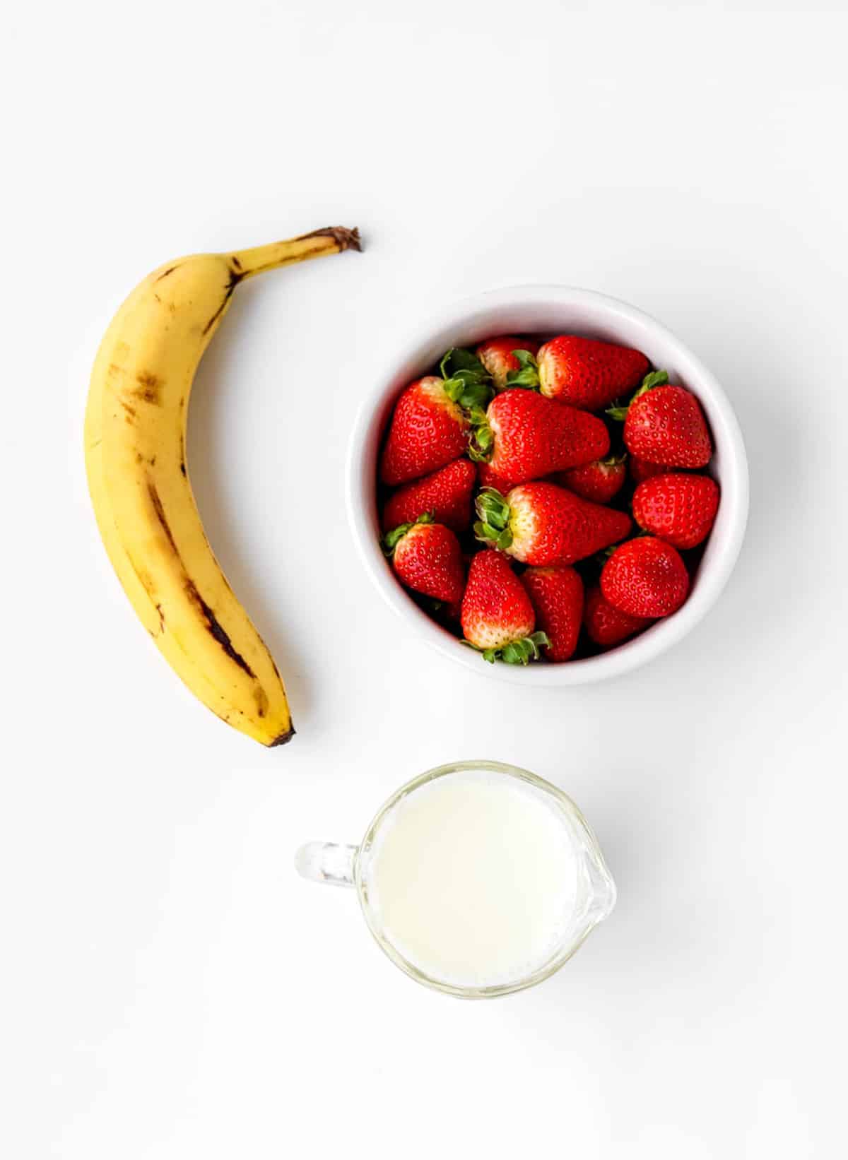A banana, strawberries and milk for the strawberry banana smoothie recipe.