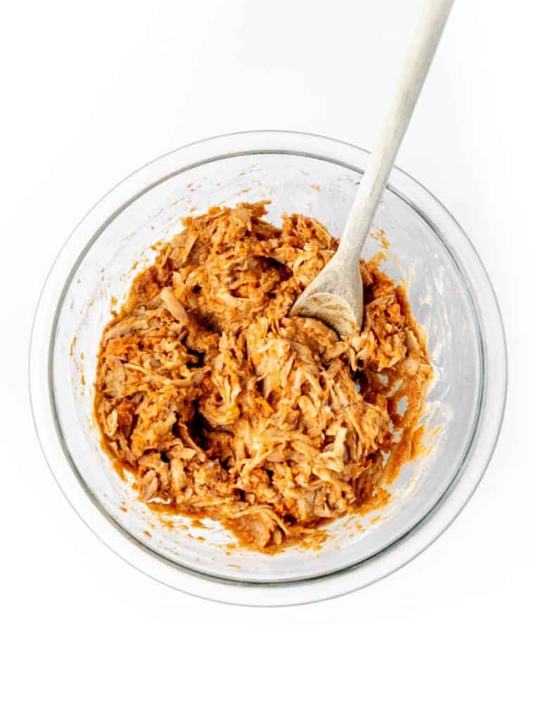 The sweet potato fritter mixture being mixed together in a bowl with a wooden spoon.