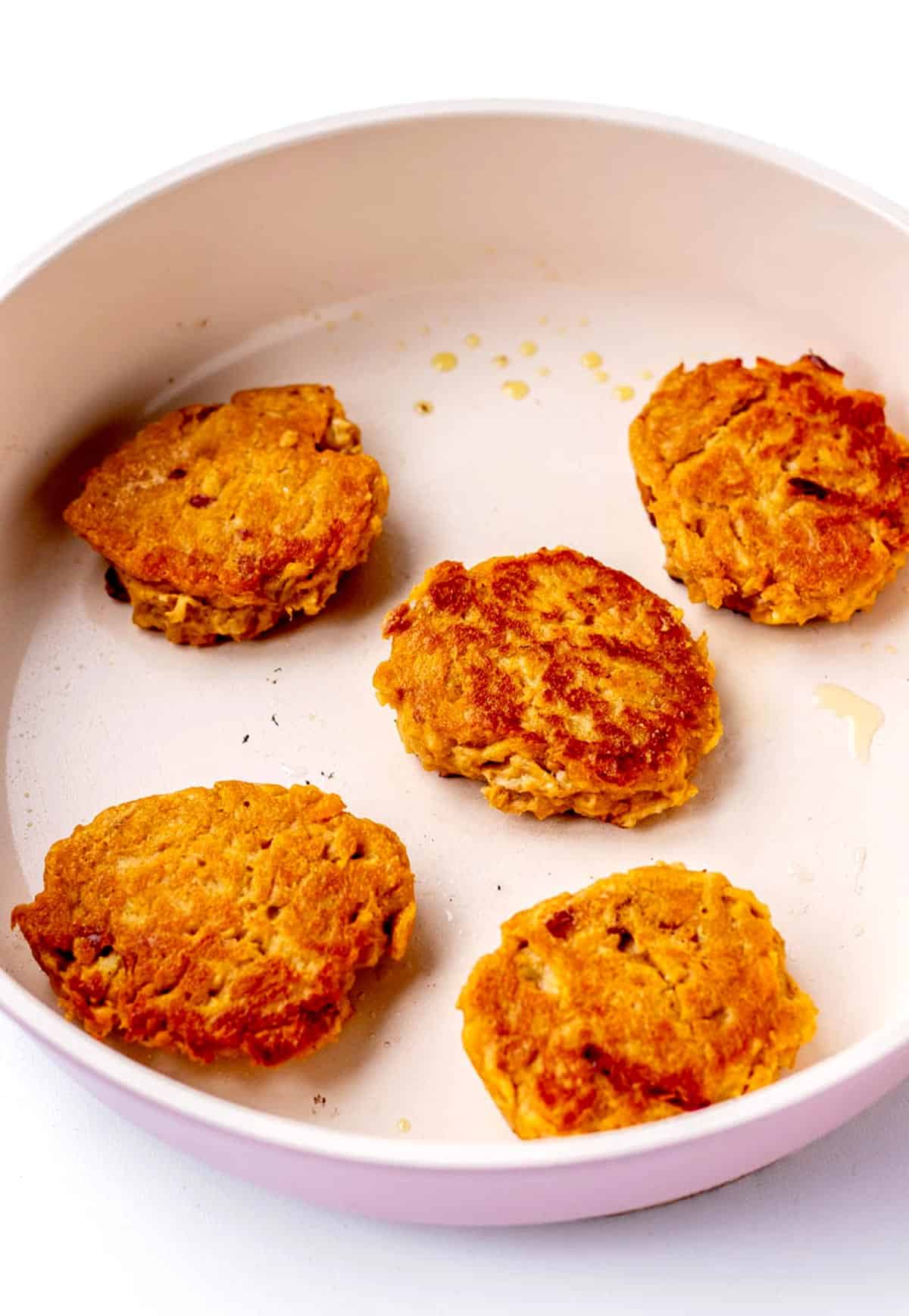 Mashed sweet potato patties cooking in a frying pan.