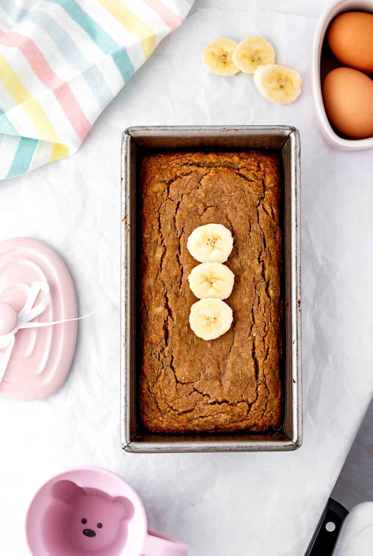 The baked baby banana bread in a loaf pan topped with banana slices.