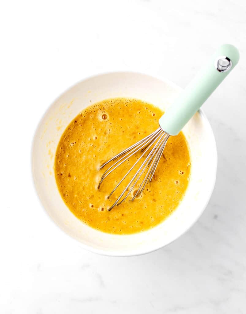 The wet ingredients being whisked in a white bowl for banana bread.