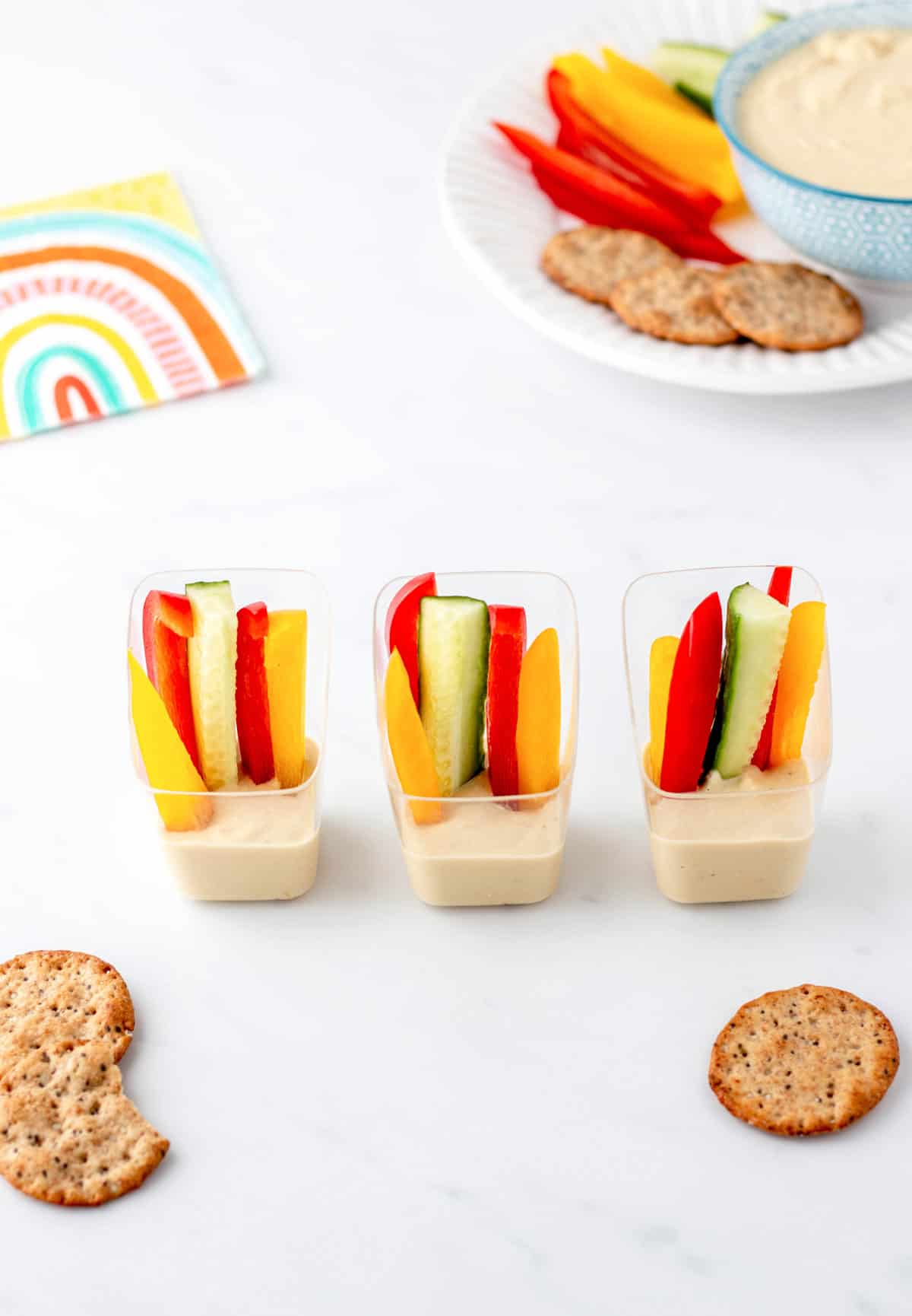 Three small clear cups with veggie sticks and Greek yogurt hummus.