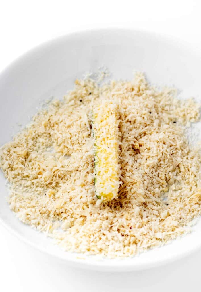 A zucchini stick being dredged in parmesan panko mixture.