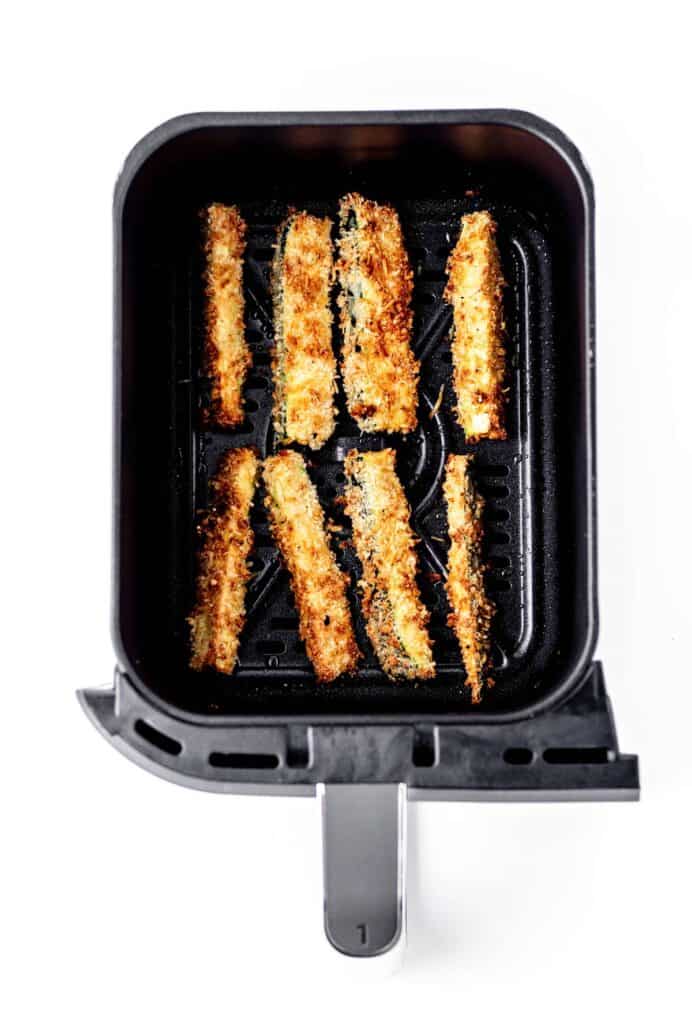 Crispy cooked zucchini fries in an air fryer basket.