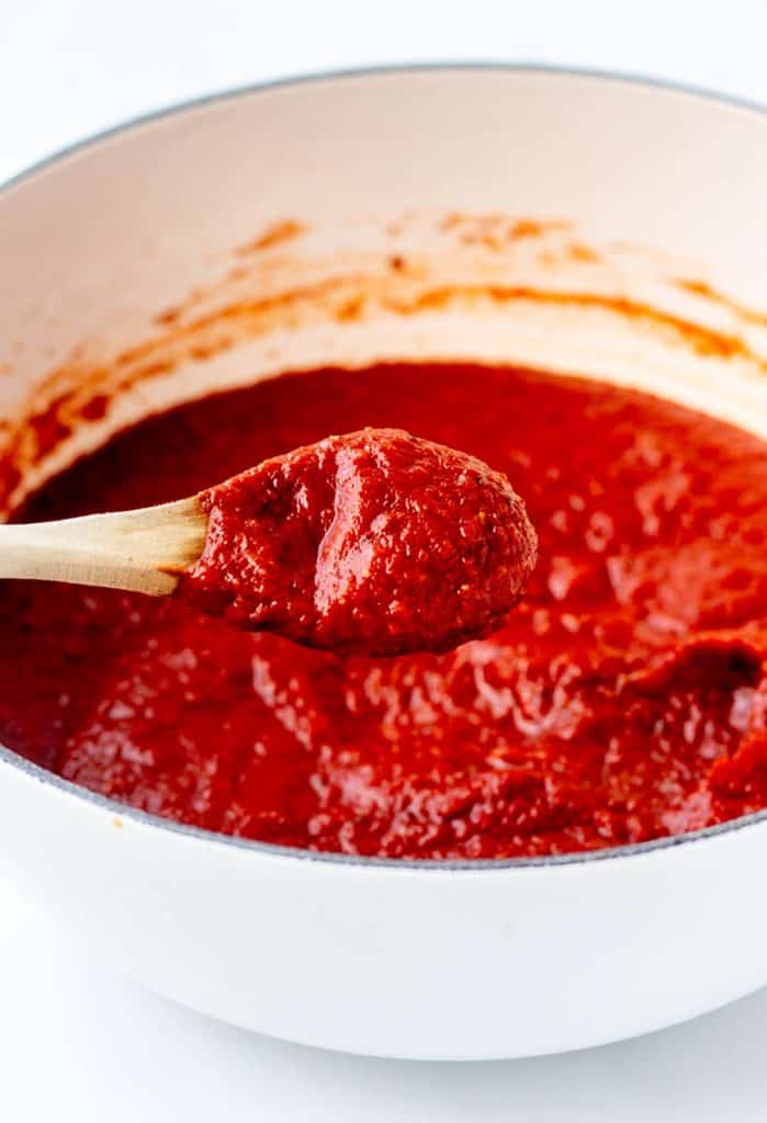 A wooden spoon holding up some homemade pizza sauce over a pot.