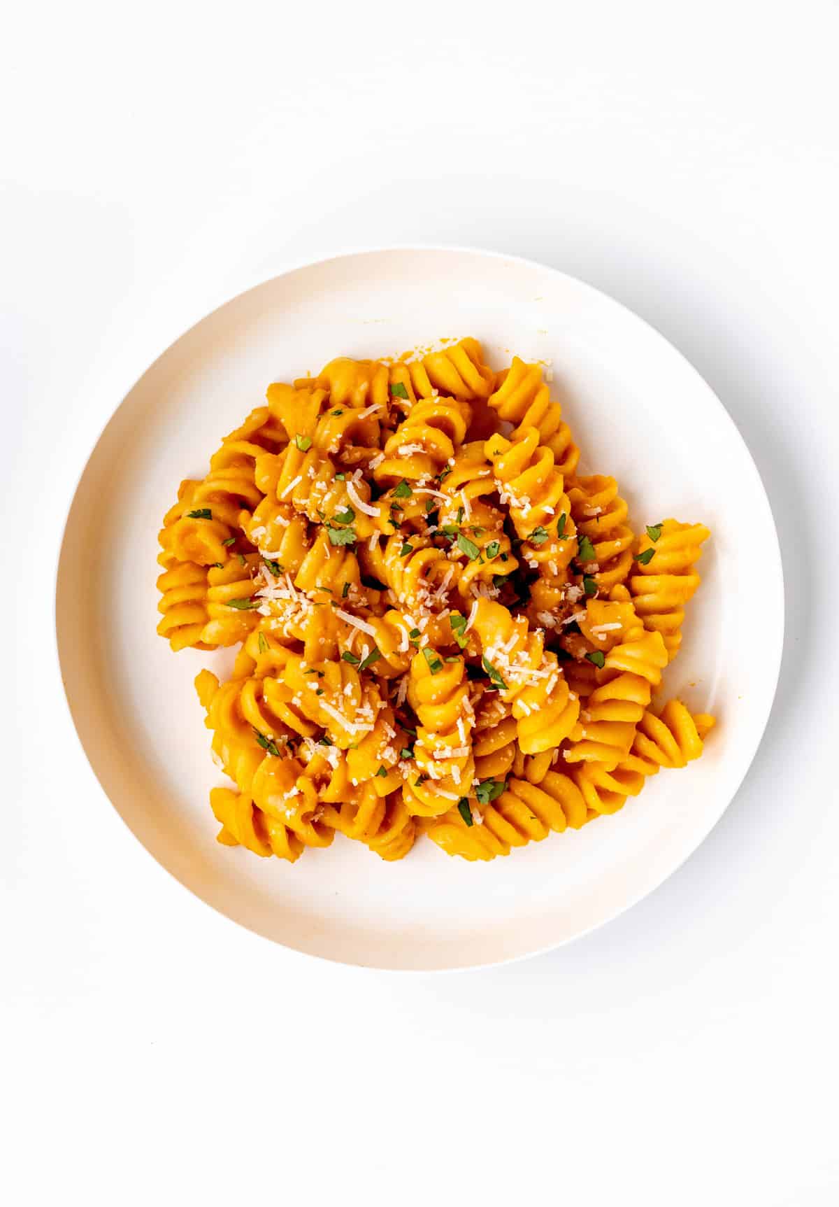 A white plate with roasted veggie pasta topped with parmesan and parsley.