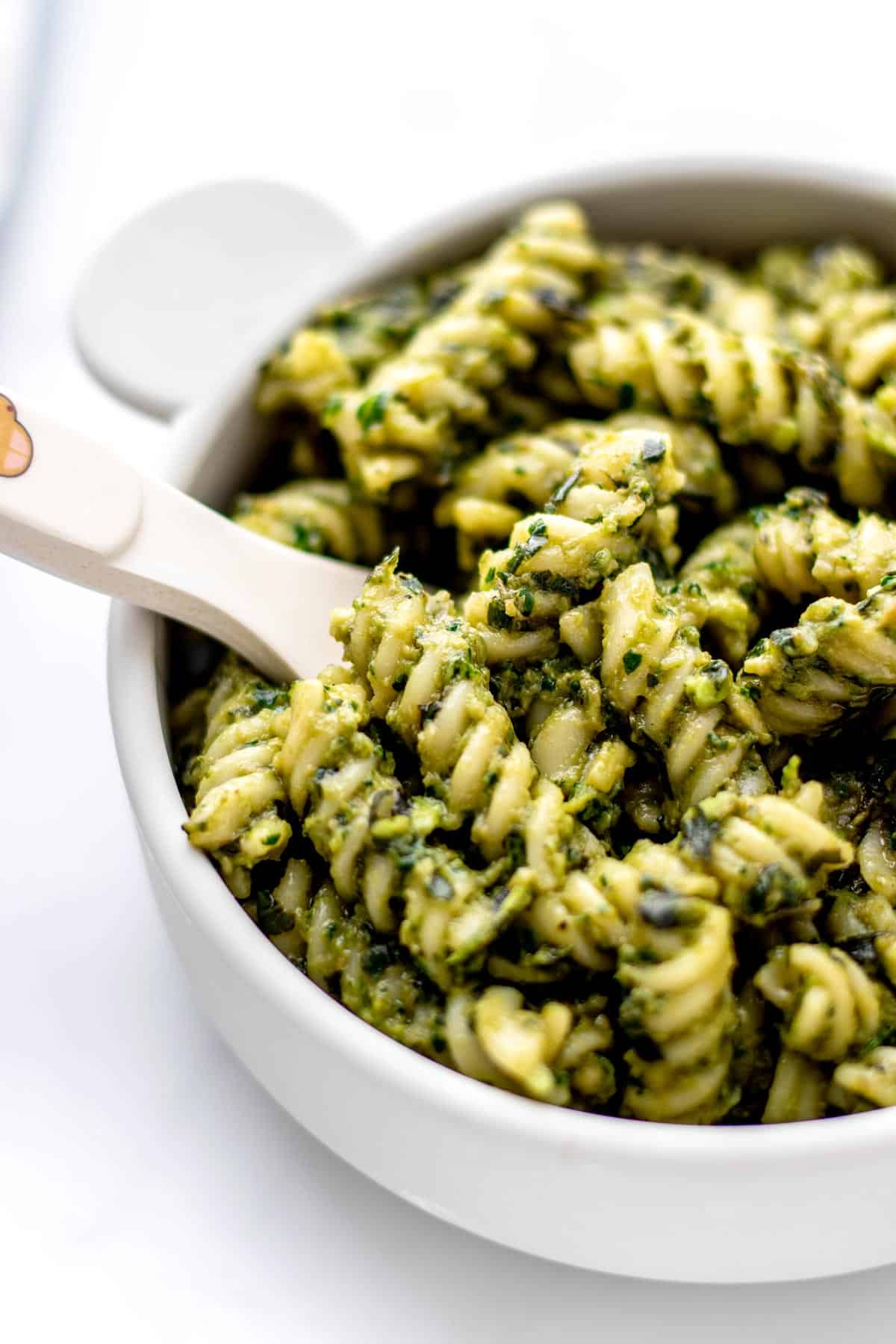 Up close image of baby pasta recipe with green sauce in a small bowl with a fork.