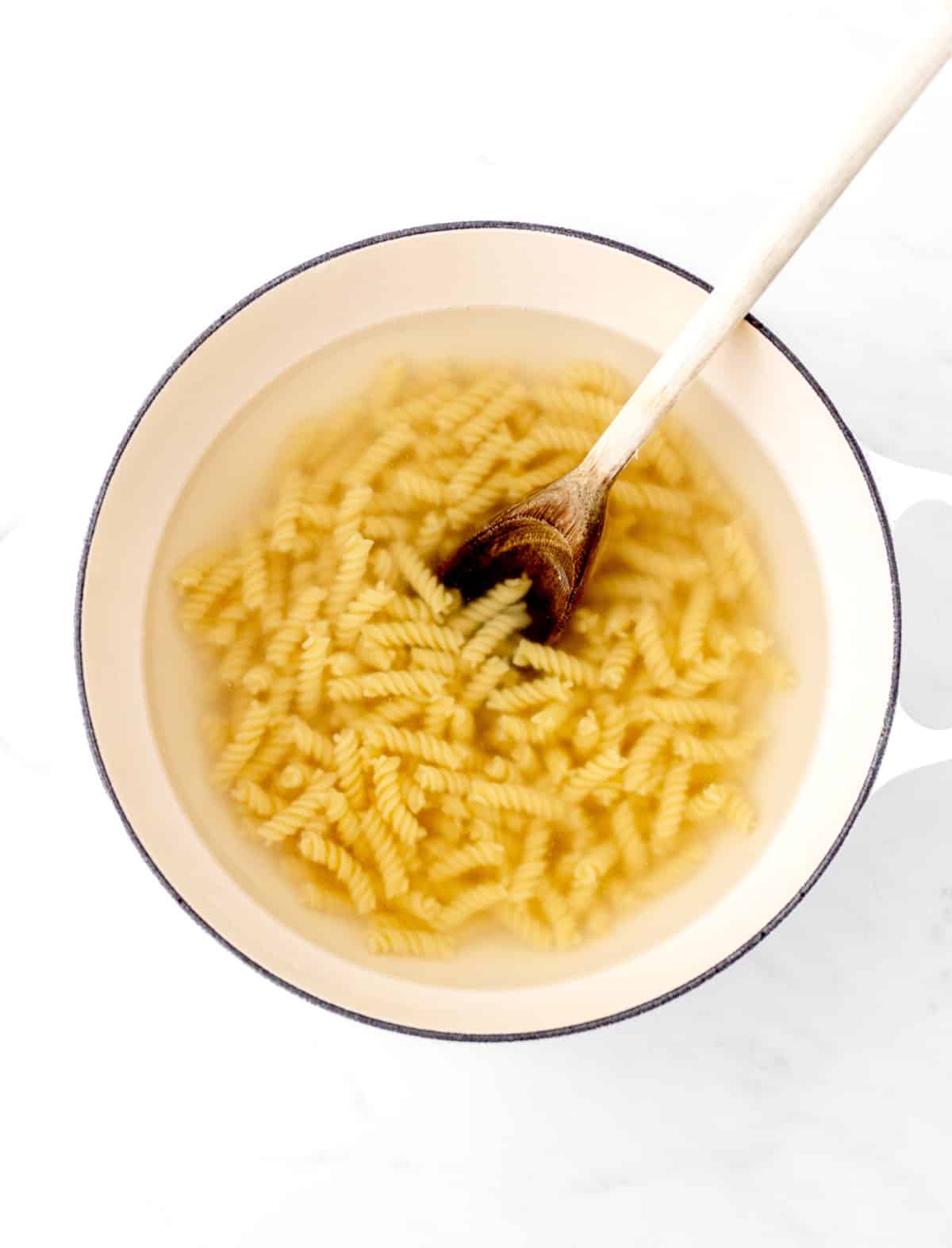 Pasta cooking in a large white pot with a wooden spoon.