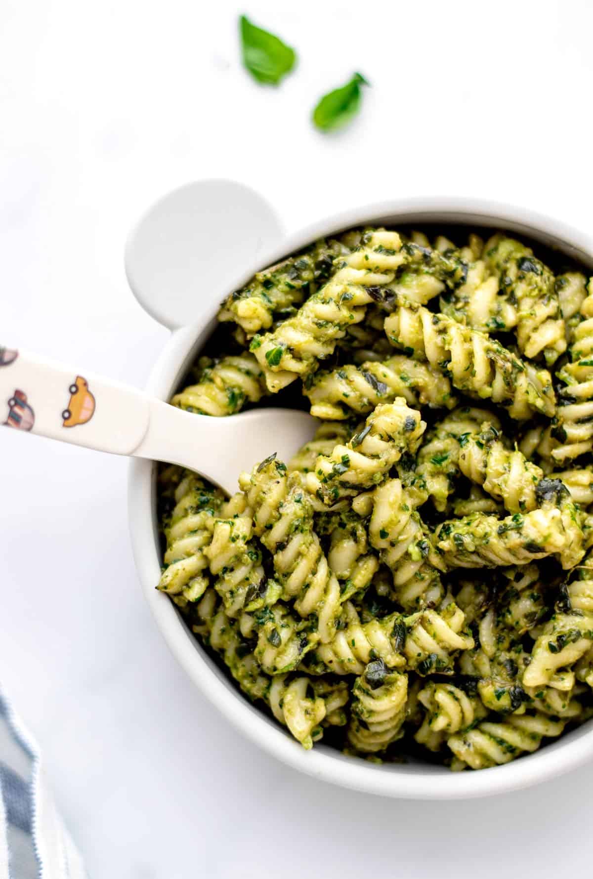 Overhead image of baby pasta in a small bowl with green sauce.