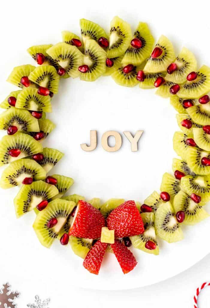 An up close Christmas fruit wreath on a large plate with holiday decorations.