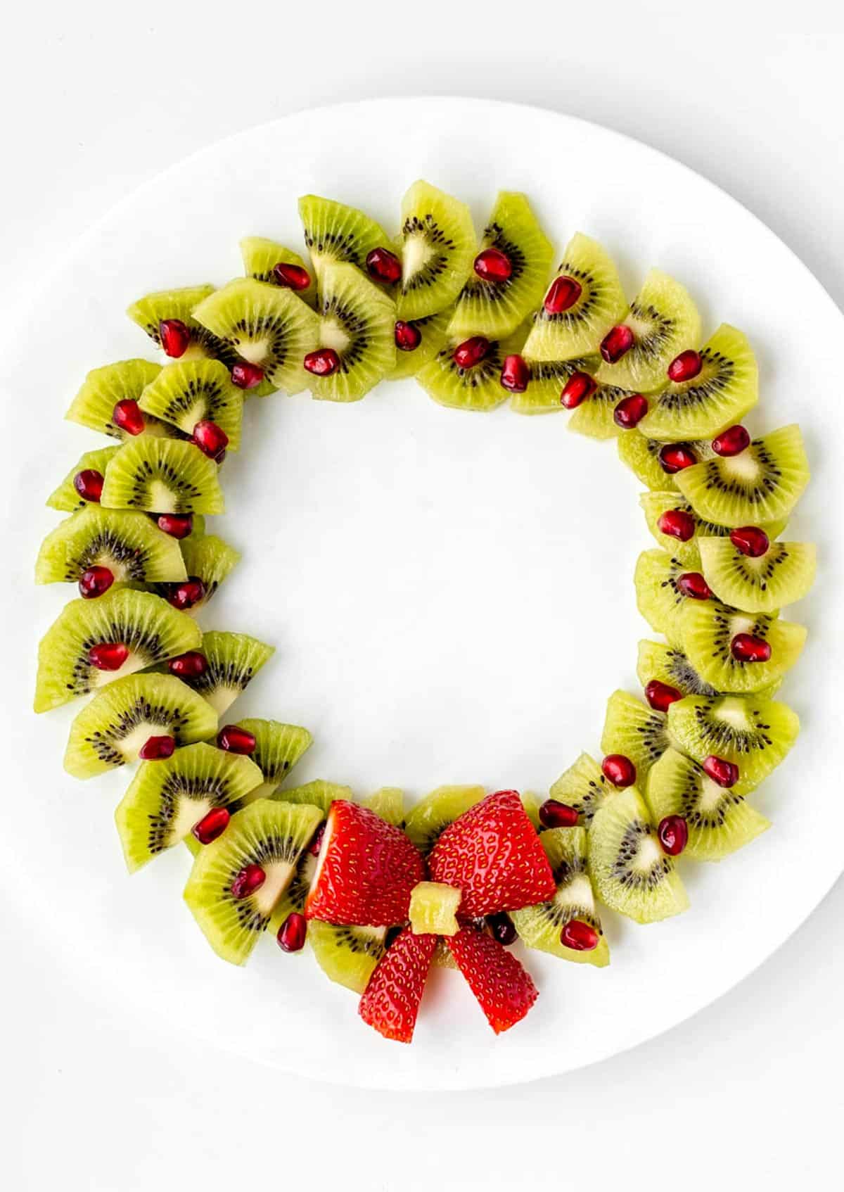 A Christmas fruit wreath on a large plate with a strawberry bow.