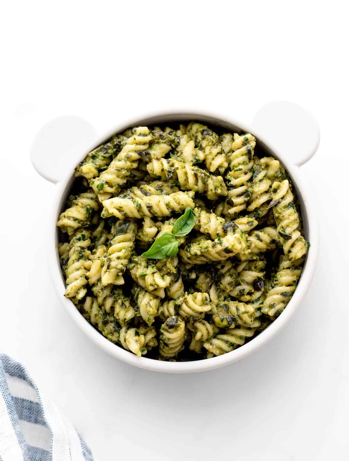 Overhead image of avocado pesto sauce mixed in with noodles in a baby bowl.