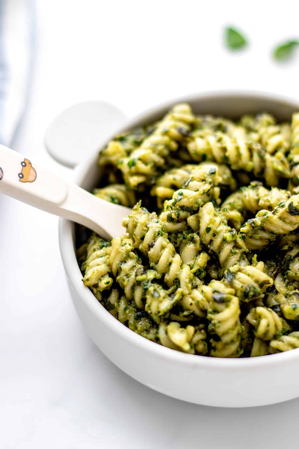 Creamy avocado pesto mixed with noodles in a small bowl with a baby fork.