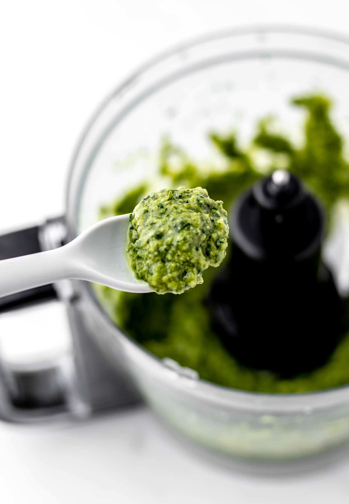 A spoon holding up some avocado pesto sauce.