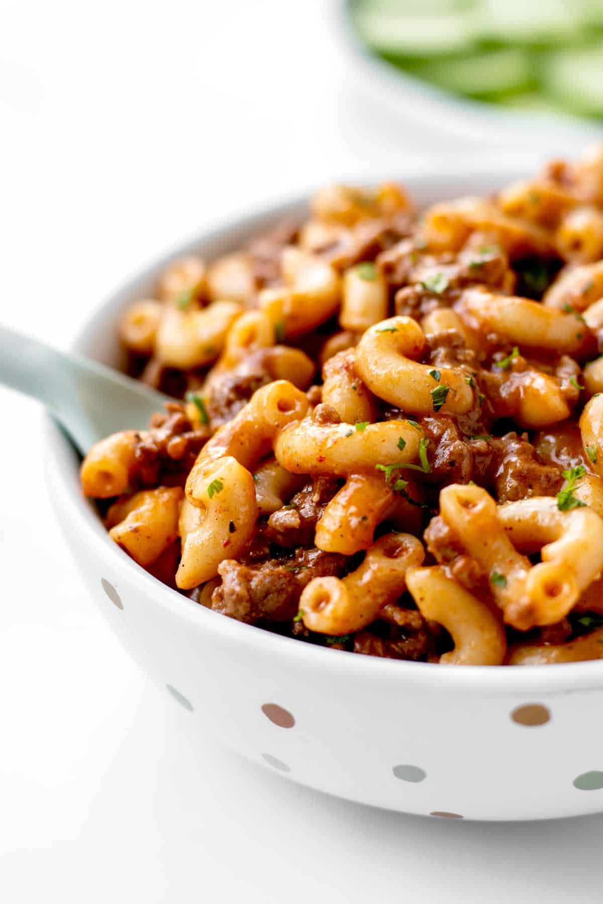 A close up image of cheeseburger macaroni in a polka dot bowl with a fork digging in.