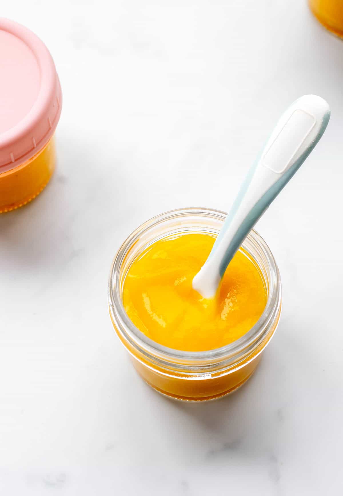 A spoon scooping up some mango puree from a baby jar.