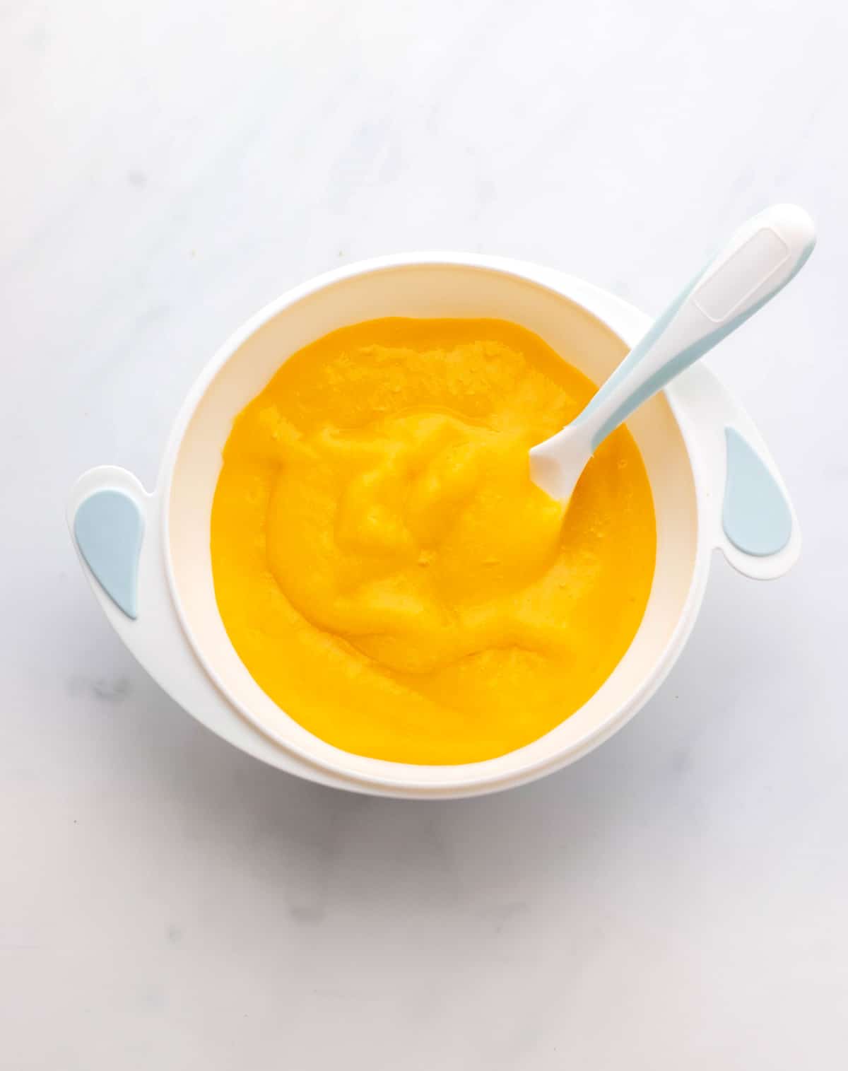 A baby spoon in a bowl with mango puree.