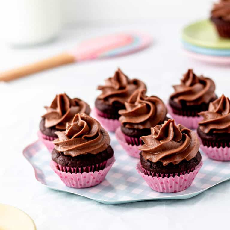 Close up image of mini chocolate cupcakes with cream cheese frosting on a blue checkered plate.