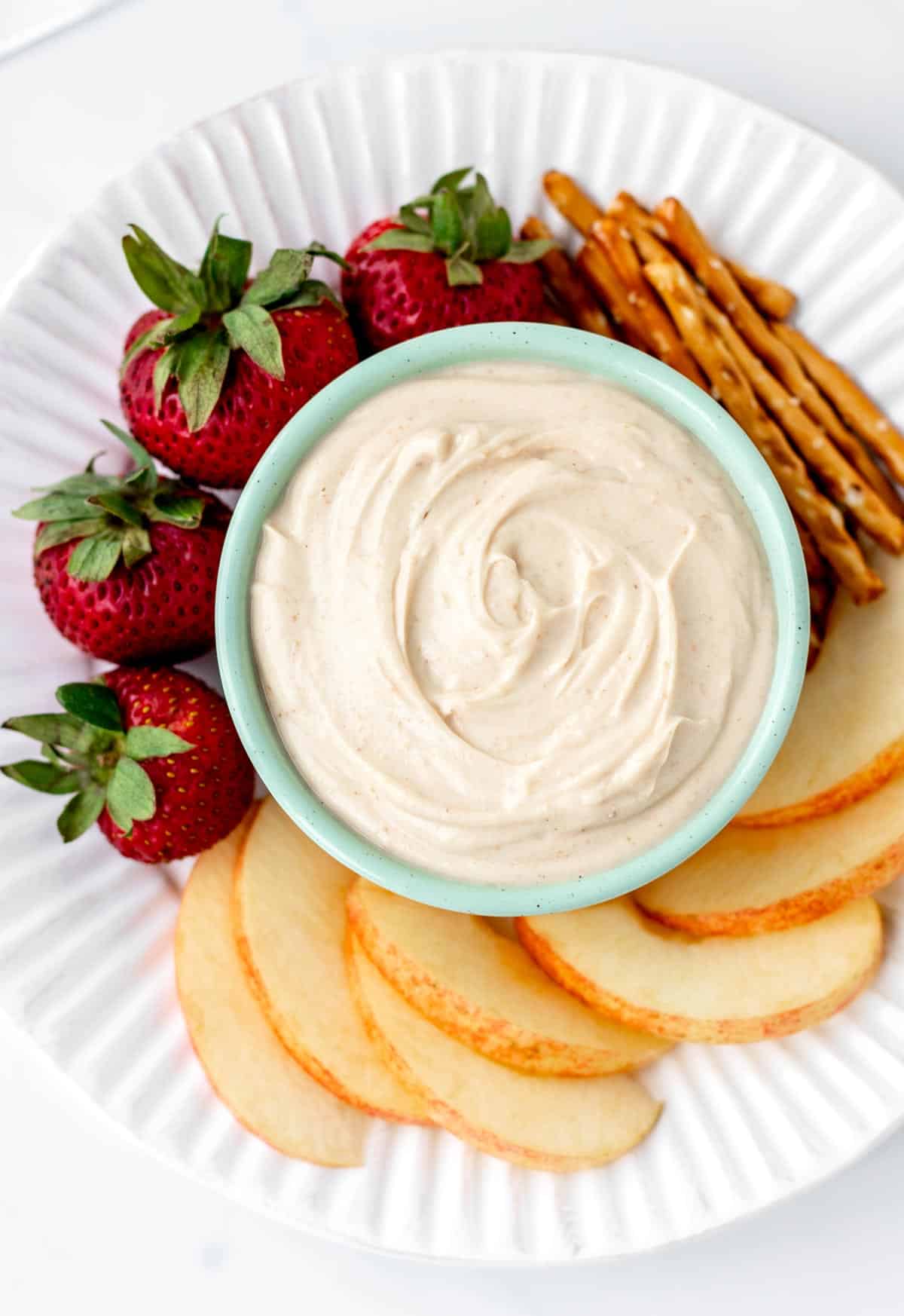 A close up image of healthy peanut butter dip with fruit and pretzels.