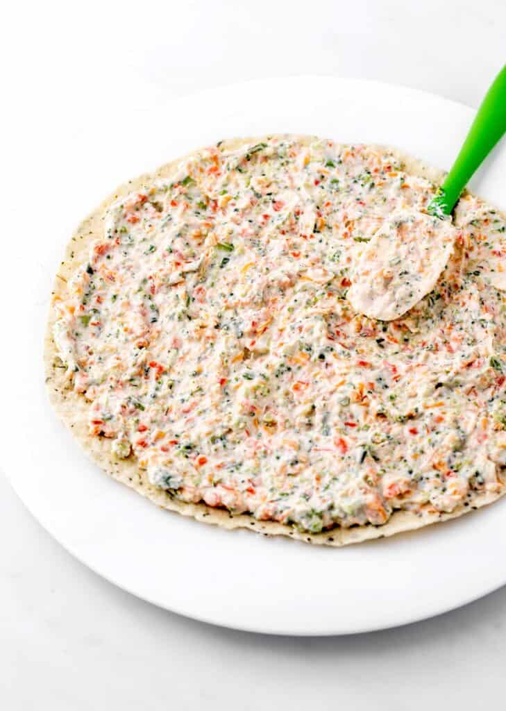 Cream cheese and veggie mixture being spread on a tortilla for veggie tortilla pinwheels.