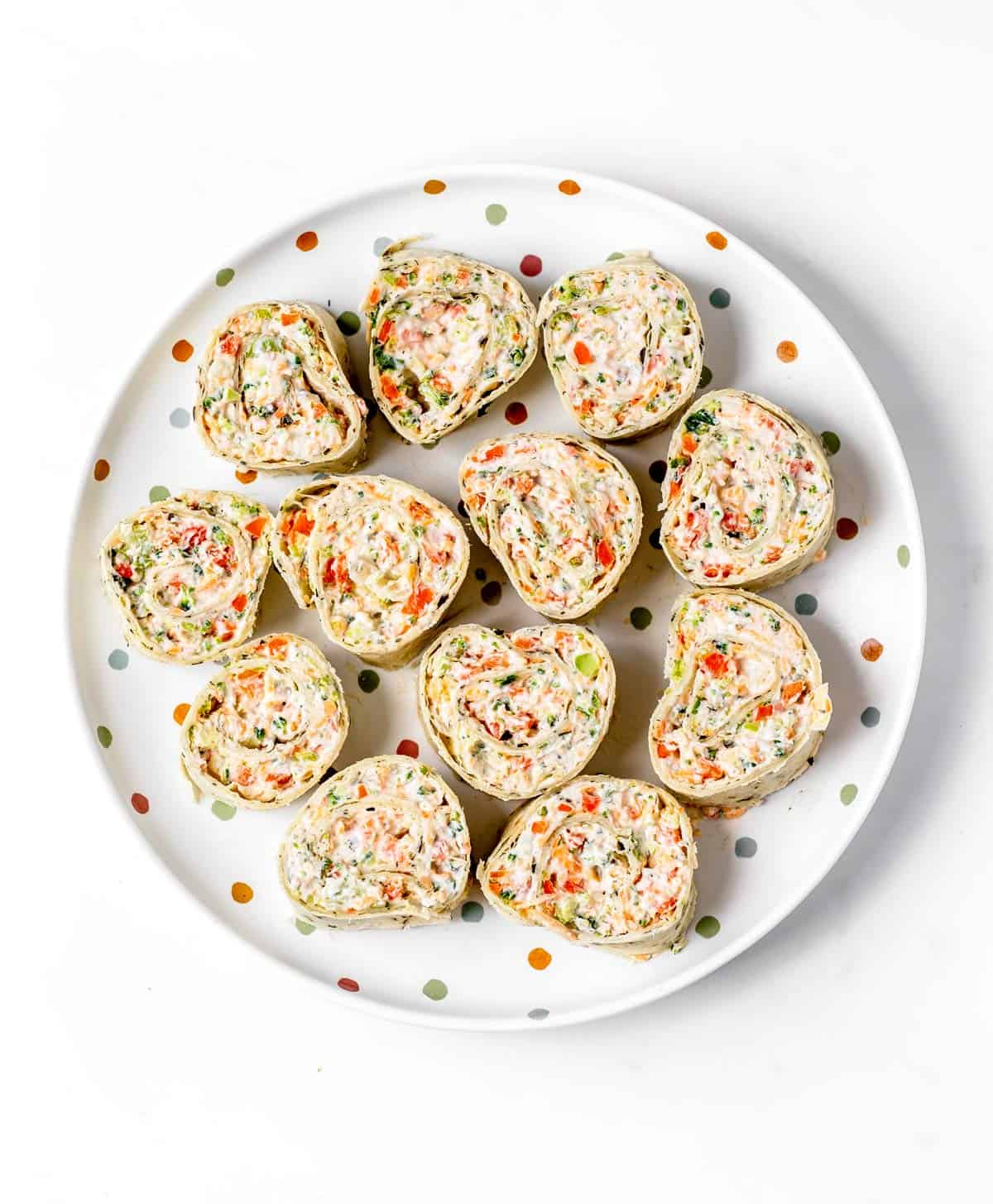 A polka dot plate with carrot, broccoli and cheese pinwheels.