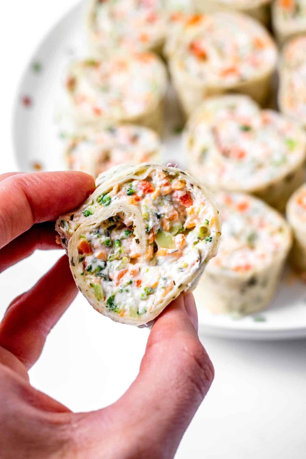 A hand holding up one of the veggie tortilla pinwheels.