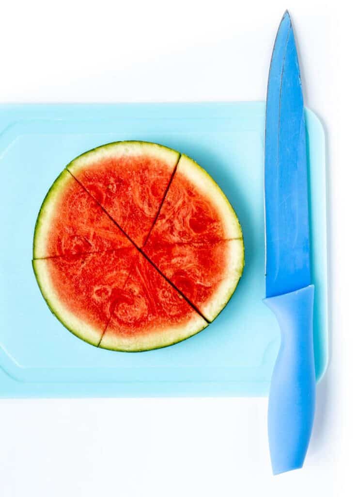 A watermelon slice cut into six triangles on a blue cutting board.